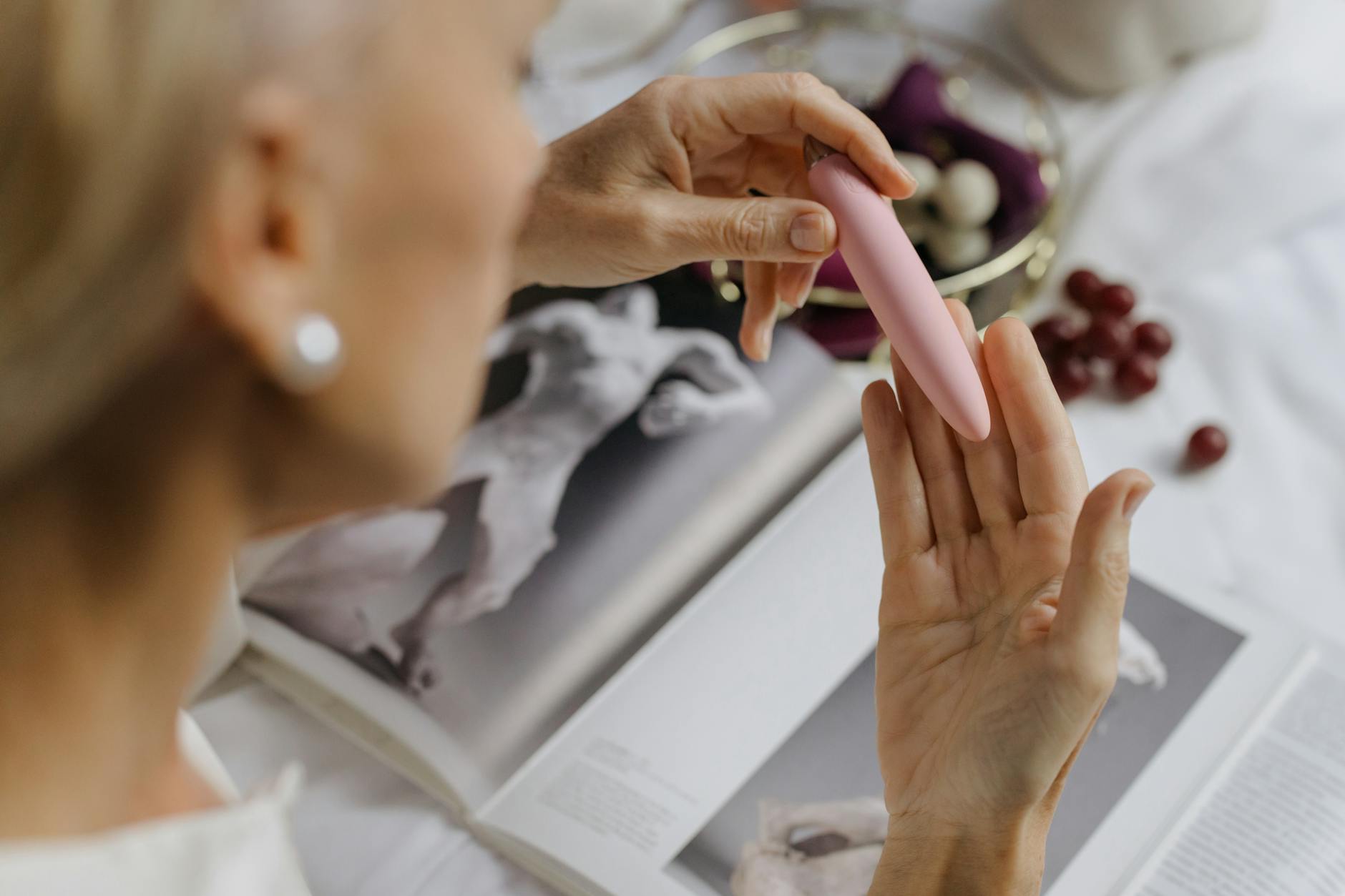 Mulher segurando um vibrador rosa, com livros de arte ao fundo, enfatizando temas íntimos e pessoais