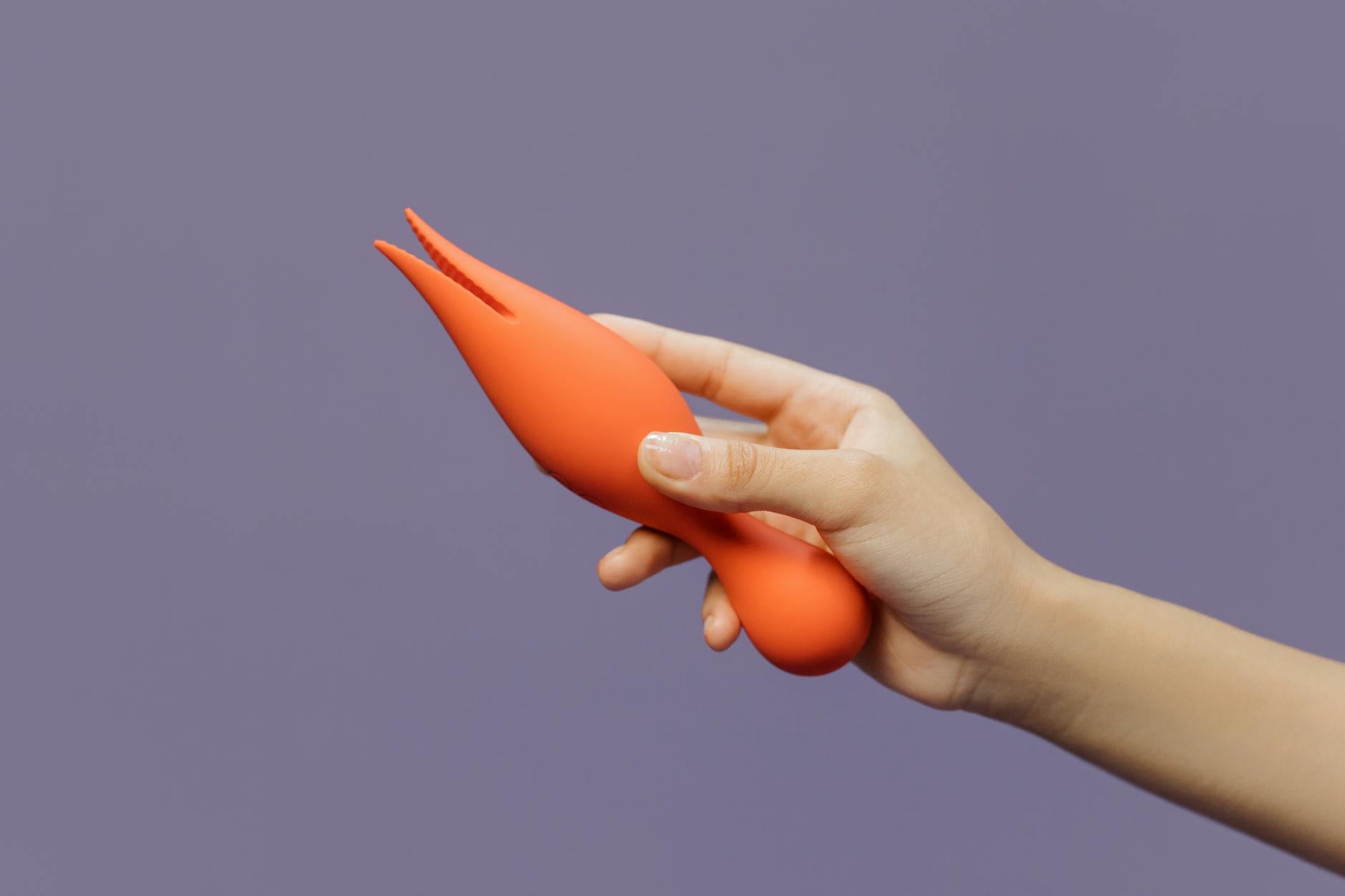 Mão segurando vibrador laranja contra fundo minimalista, representando sexualidade moderna e recuperação de intimidade