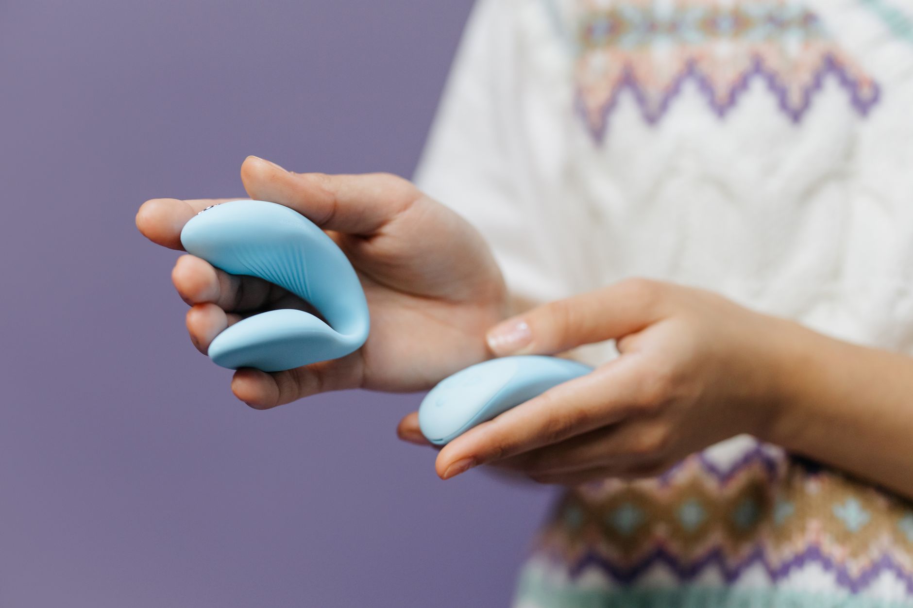 Mão segurando um vibrador azul contra um fundo roxo minimalista.