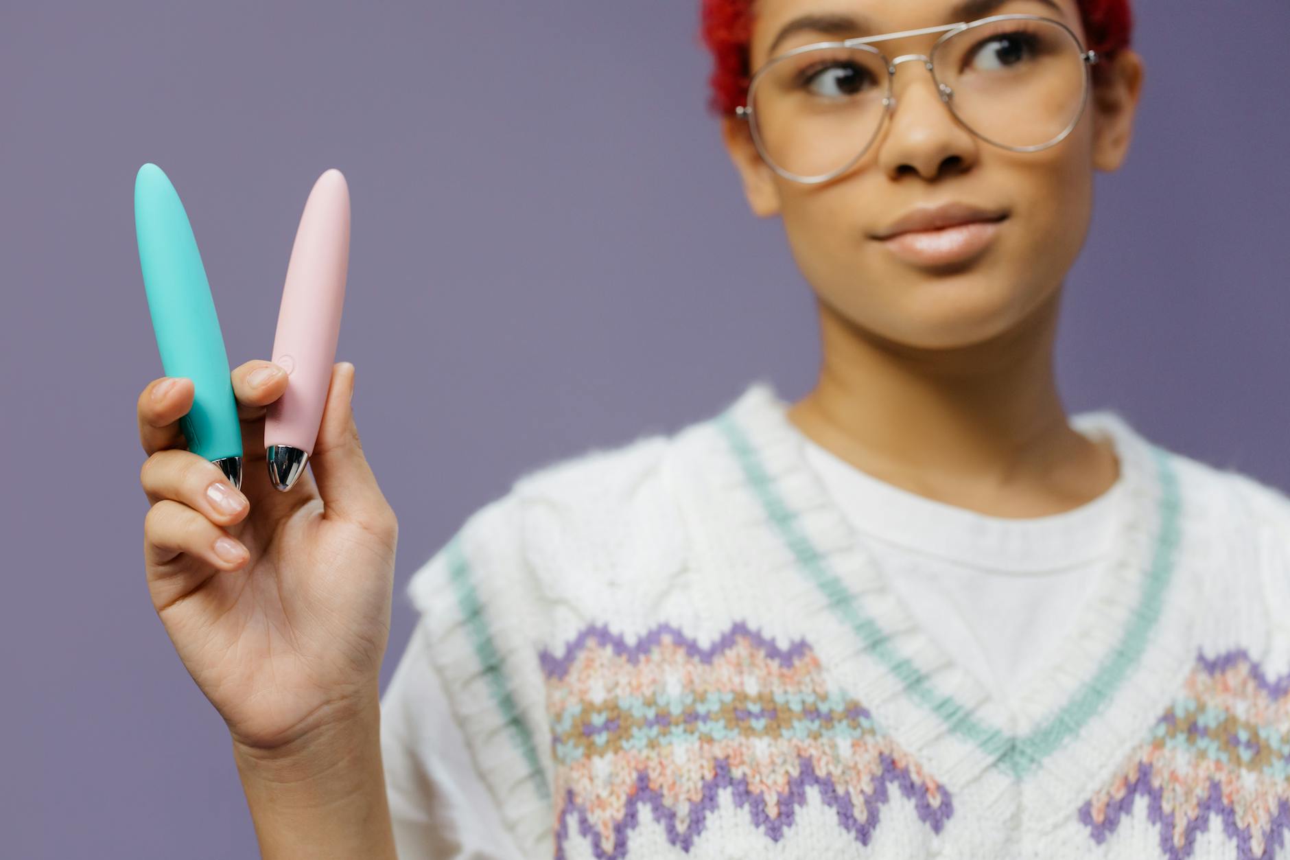 Mulher jovem segurando vibradores coloridos contra fundo roxo, representando escolha segura e controle
