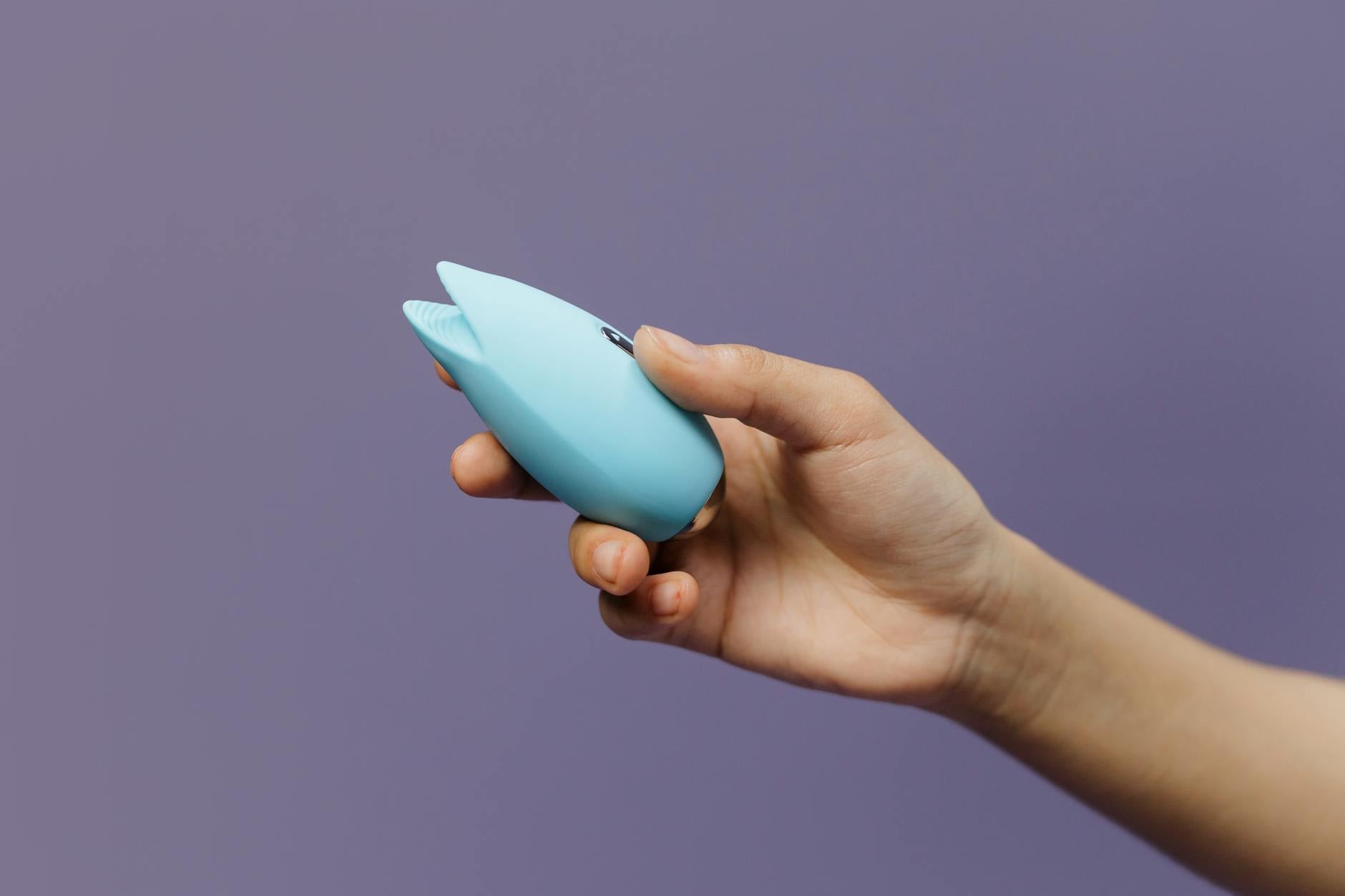 Mão de uma mulher alcançando uma variedade de brinquedos sexuais coloridos sobre uma mesa
