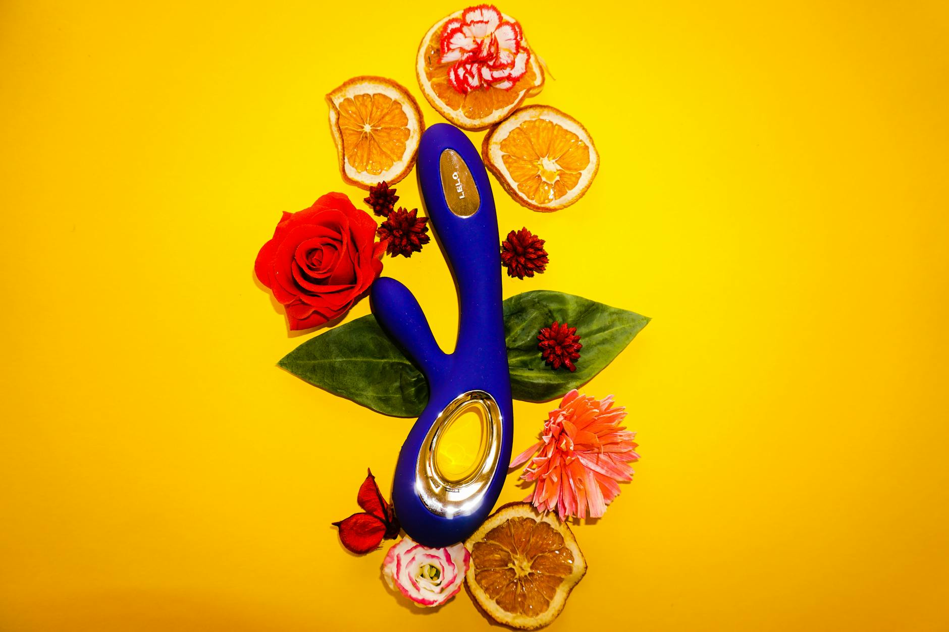 Vibrador de limão azul cercado por flores e fatias de laranja em fundo amarelo